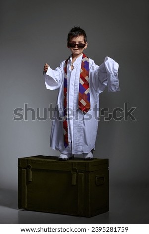 little boy in very large sneakers and a very large white shirt and tie posing cheerfully in the studio