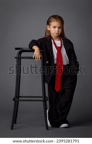 little girl in a black pantsuit and red tie posing in the studio