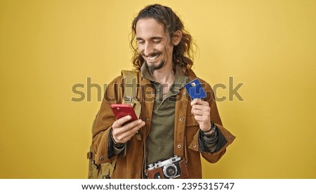 Young hispanic man tourist shopping with credit card and smartphone over isolated yellow background
