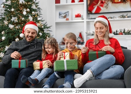 Happy family in Santa hats with Christmas gifts on sofa at home