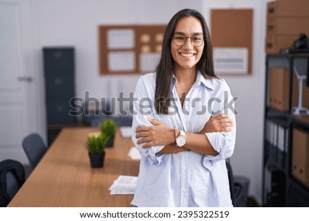 Young hispanic woman at the office happy face smiling with crossed arms looking at the camera. positive person.  Royalty-Free Stock Photo #2395322519