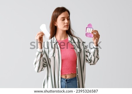 Young woman with box of tampons and menstrual pad on light background Royalty-Free Stock Photo #2395326587