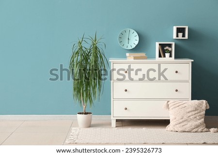 Chest of drawers with decor and houseplant near color wall