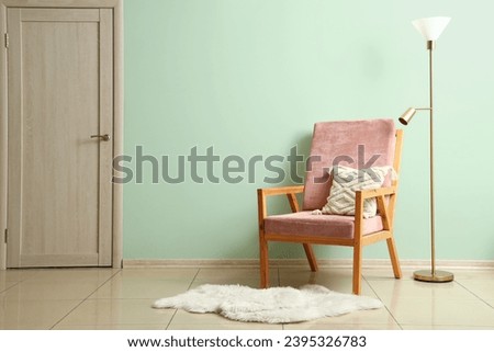 Pink wooden armchair with lamp near green wall in room Royalty-Free Stock Photo #2395326783
