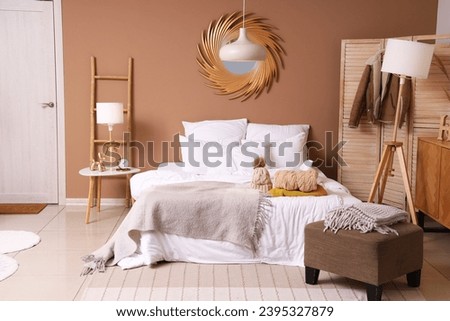 Interior of cozy bedroom with winter clothes on bed and lamps Royalty-Free Stock Photo #2395327879
