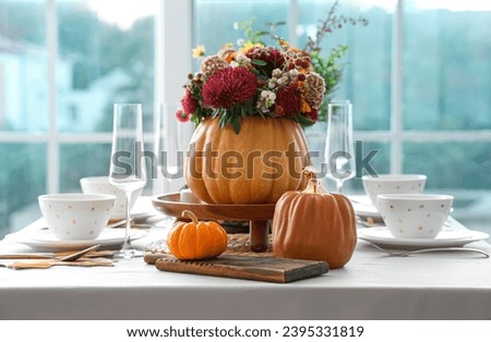 Beautiful bouquet of autumn flowers in pumpkin on festive dining table