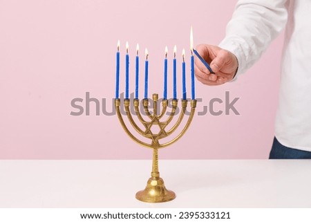 Man lighting candles in menorah on pink background, closeup. Hanukkah celebration