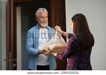 Helping neighbours. Young woman with net bag of products visiting senior man outdoors Royalty-Free Stock Photo #2395333535
