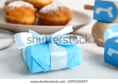 Gift box, dreidels and donuts for Hanukkah celebration on light background, closeup