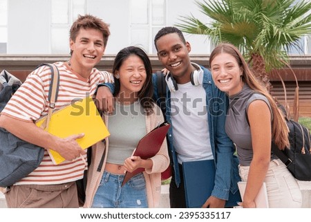 Group of multicultural university students smiling and looking at camera holding folders and notebooks with backpacks. Youth friends together posing for a photo outside the campus