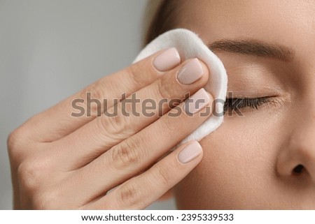 Woman removing makeup with cotton pad on grey background, closeup Royalty-Free Stock Photo #2395339533