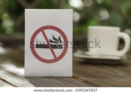 No Smoking sign and cup of drink on wooden table against blurred background, closeup