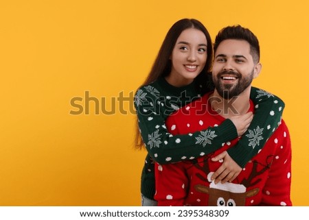 Happy young couple in Christmas sweaters on orange background. Space for text