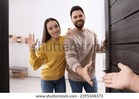 Happy couple welcoming their guest near door. Invitation to come indoors Royalty-Free Stock Photo #2395348373