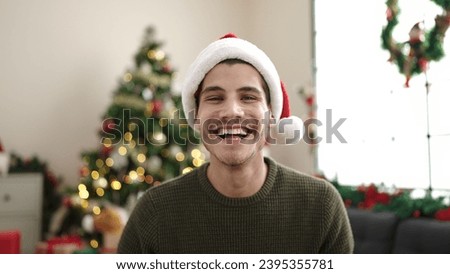 Young hispanic man smiling confident sitting on sofa by christmas tree at home