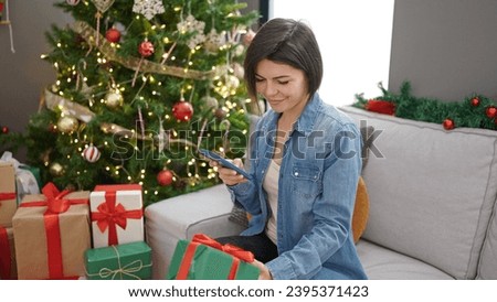 Young caucasian woman taking photo of present sitting by christmas tree at home
