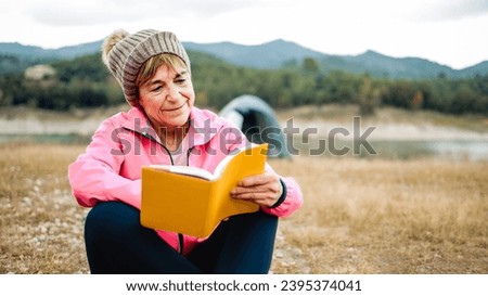 Happy senior woman reading a book outdoors during hiking day. Adventure and travel vacations concept Royalty-Free Stock Photo #2395374041