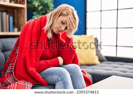 Young blonde woman suffering for headache sitting on sofa at home Royalty-Free Stock Photo #2395374813
