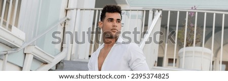 cuban man with curly hair and in white shirt looking away on urban street in Miami, banner