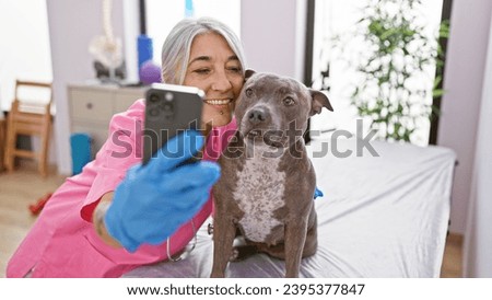 Smiling middle-aged veterinarian adorably taking selfie with a senior dog at vet clinic, immersed in the world of pet health care