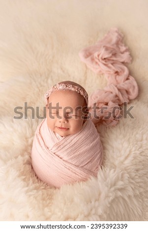 Sleeping newborn girl in the first days of life in a white cocoon with a white bandage on a white background. Studio macro photography, portrait of a newborn. The concept of female happiness.  Royalty-Free Stock Photo #2395392339