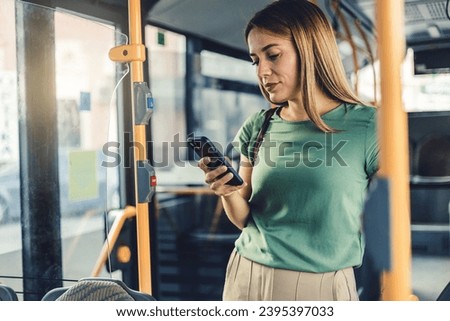 Young woman checking social media on phone in bus. Beautiful girl with long hair using smartphone for reading or writing message while standing in city bus.