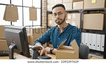 Young hispanic man ecommerce business looking serious at the camera at office