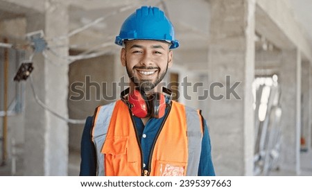 Young hispanic man builder smiling confident wearing hardhat at construction site Royalty-Free Stock Photo #2395397663