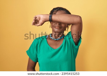 African woman with dreadlocks standing over yellow background covering eyes with arm, looking serious and sad. sightless, hiding and rejection concept  Royalty-Free Stock Photo #2395415253