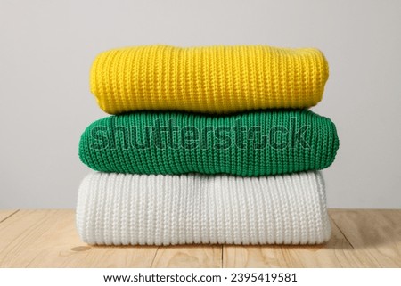 Stack of casual sweaters on wooden table against light background Royalty-Free Stock Photo #2395419581