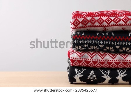 Stack of different Christmas sweaters on table against light background. Space for text