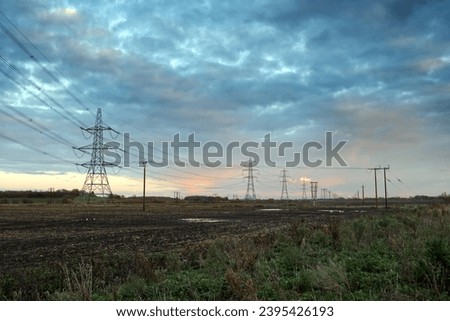 Wide angle of electrical power lines at dusk with a blue and pink sky. The lines lead away across a muddy field, to a vanishing point in the distance. Royalty-Free Stock Photo #2395426193