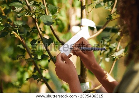 Close up of woman gardener signs the names of the plants in botanic center