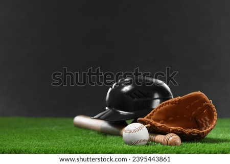 Baseball bat, batting helmet, leather glove and ball on green grass against dark background. Space for text