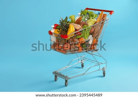 Shopping cart full of groceries on light blue background Royalty-Free Stock Photo #2395445489