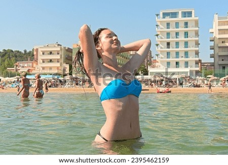 A young woman in a bikini adjusting wet hair on an urban beach