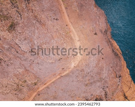 Curved path on cliff with group of small people and blue ocean water. Abstract picture. Aerial top view.