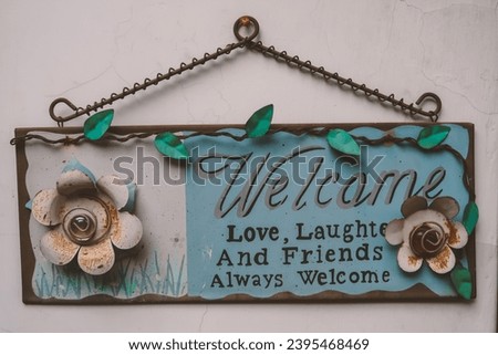 A welcoming board sign hanging on the white wall, written love laughs and friends always welcome with flowers and leaves as decoration