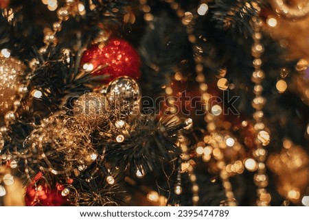 Golden garland lights and shiny gold red Christmas balls hanging on a Christmas tree. Decorated spruce branches