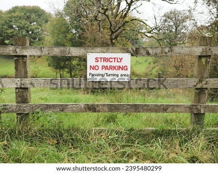 Close-up of a wooden fence with two signs that read "Strictly No Parking in This Field" prominently displayed