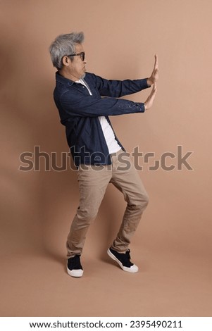 Asian energetic senior man with glasses posing  isolated on the brown background with casual clothes. mature man, Asian man. Elderly,  studio shot. Multiple emotions.