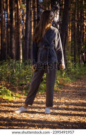 Blonde woman looks around and explores forest nature against trees. Lady enjoys walking in illuminated autumn forest and poses in tree shadow