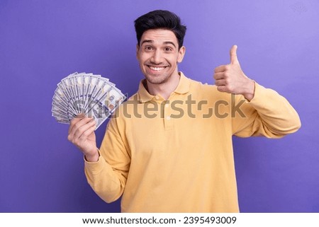 Photo of cool confident man dressed yellow shirt rising dollars fan showing thumb up isolated purple color background
