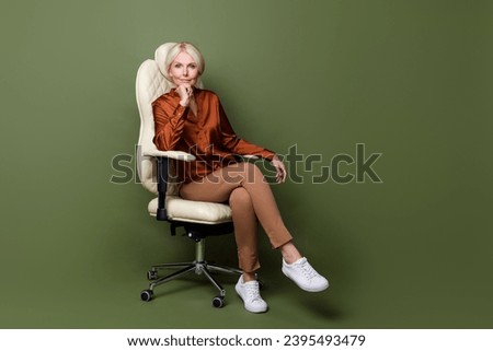 Full body photo of attractive pensioner woman think listen armchair wear trendy brown satin clothes isolated on khaki color background