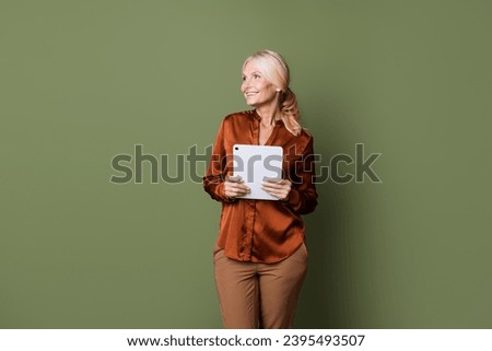 Photo portrait of pretty retired female look empty space hold tablet wear trendy brown satin outfit isolated on khaki color background