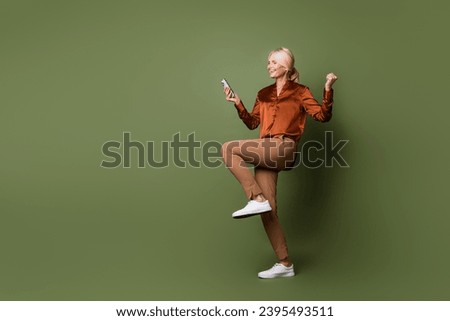 Full size photo of overjoyed ecstatic person wear trendy blouse brown pants look at smartphone win bet isolated on khaki color background