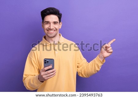 Photo of positive cheerful guy wear yellow polo typing modern gadget pointing empty space isolated violet color background