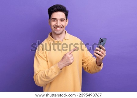 Photo of positive charming man dressed yellow shirt pointing apple iphone samsung modern device isolated purple color background