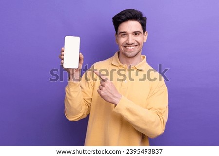 Photo of funky good mood guy wear yellow polo pointing finger modern device empty space isolated violet color background