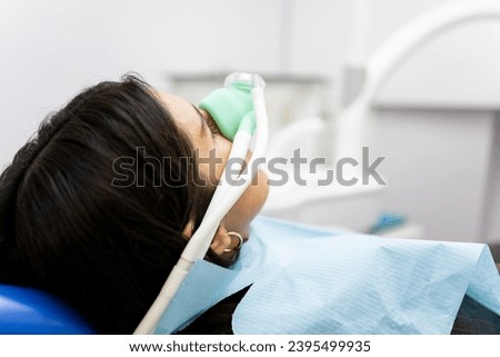 An adult woman sits in a dentist's clinic wearing a nasal mask to inhale nitrous oxide. Dentist fear concept. Feeling of relaxation with laughing gas. Royalty-Free Stock Photo #2395499935